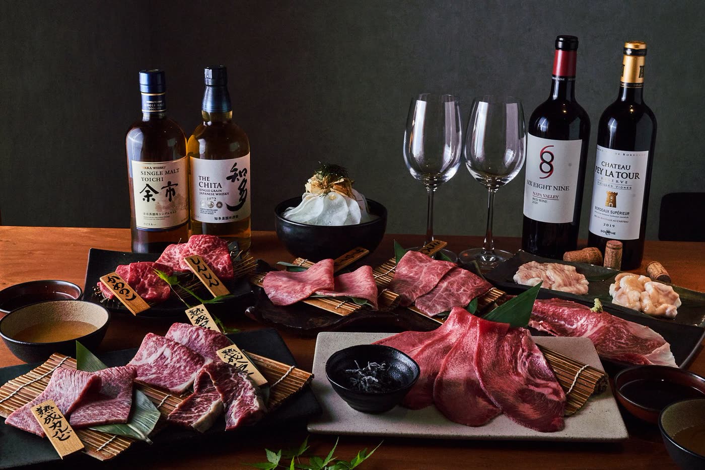 黒い天板に並べた和牛と日本酒。斜めからの光で肉の脂と器の質感が浮き上がっている