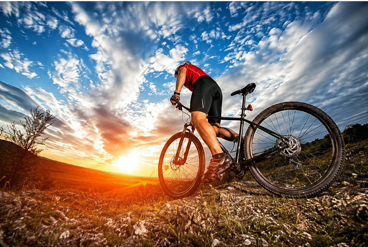 夕暮れの丘を自転車で走る人。空が大きく写り込んでいる